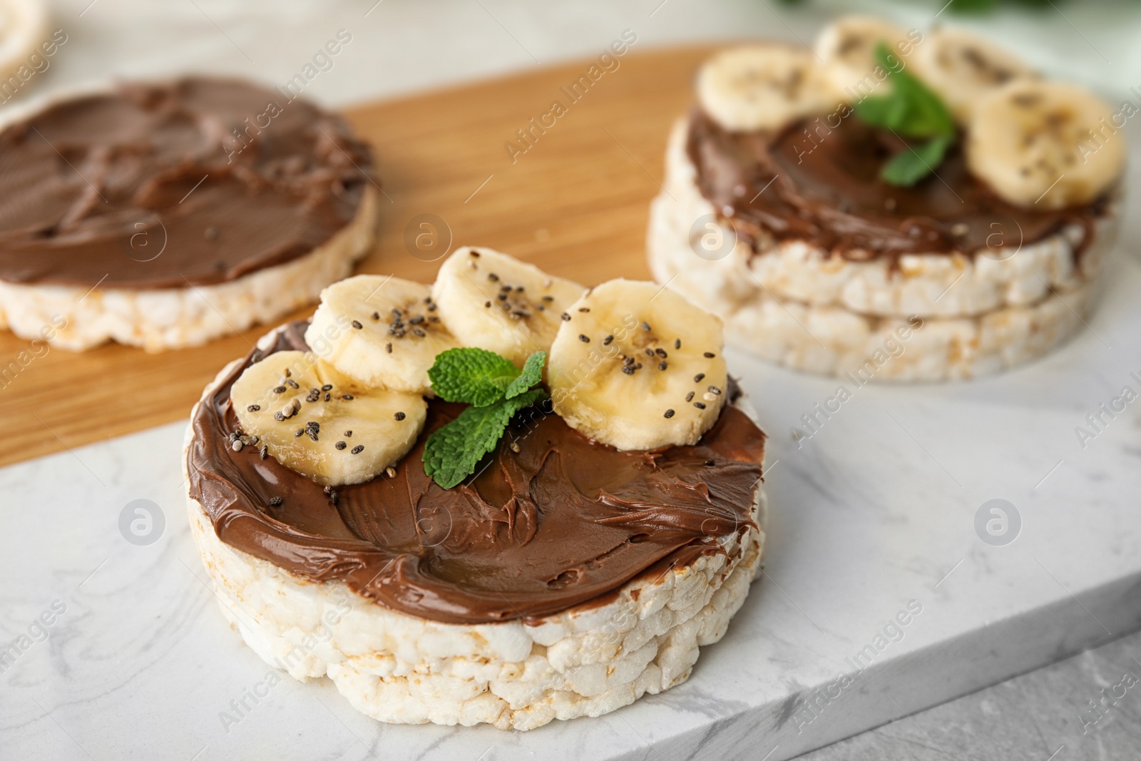 Photo of Puffed rice cakes with chocolate spread, banana and mint on board, closeup