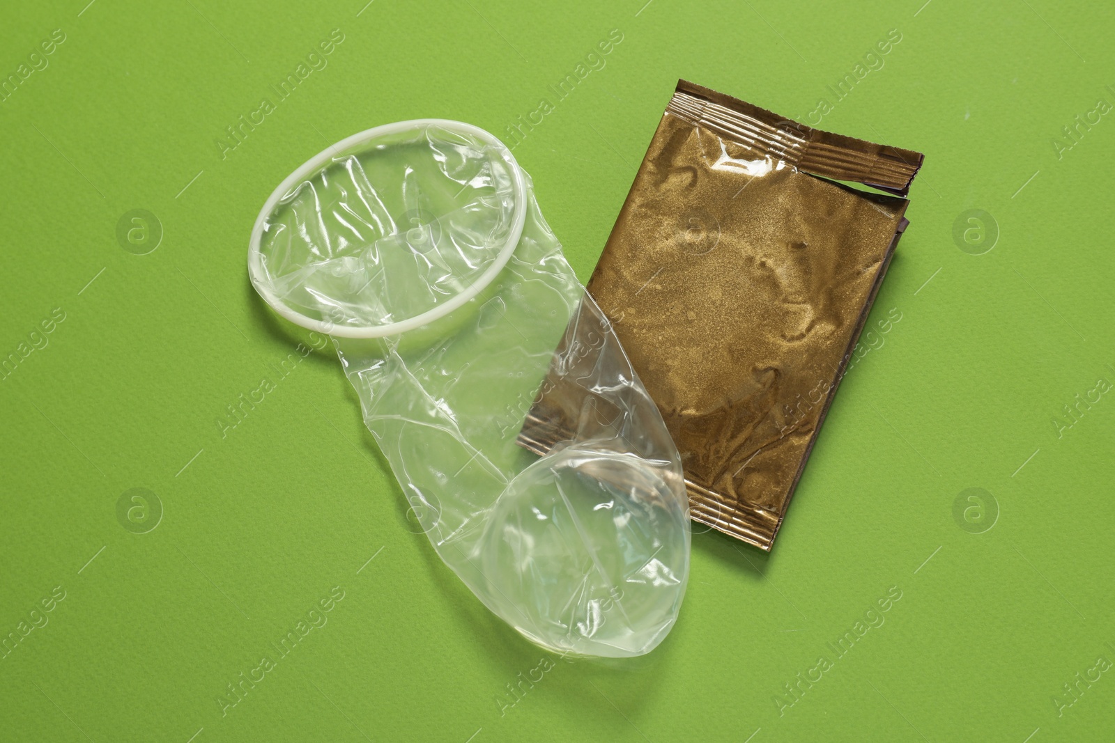 Photo of Unrolled female condom and torn package on green background, above view. Safe sex