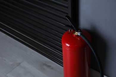 Photo of Fire extinguisher near grey wall indoors. Space for text
