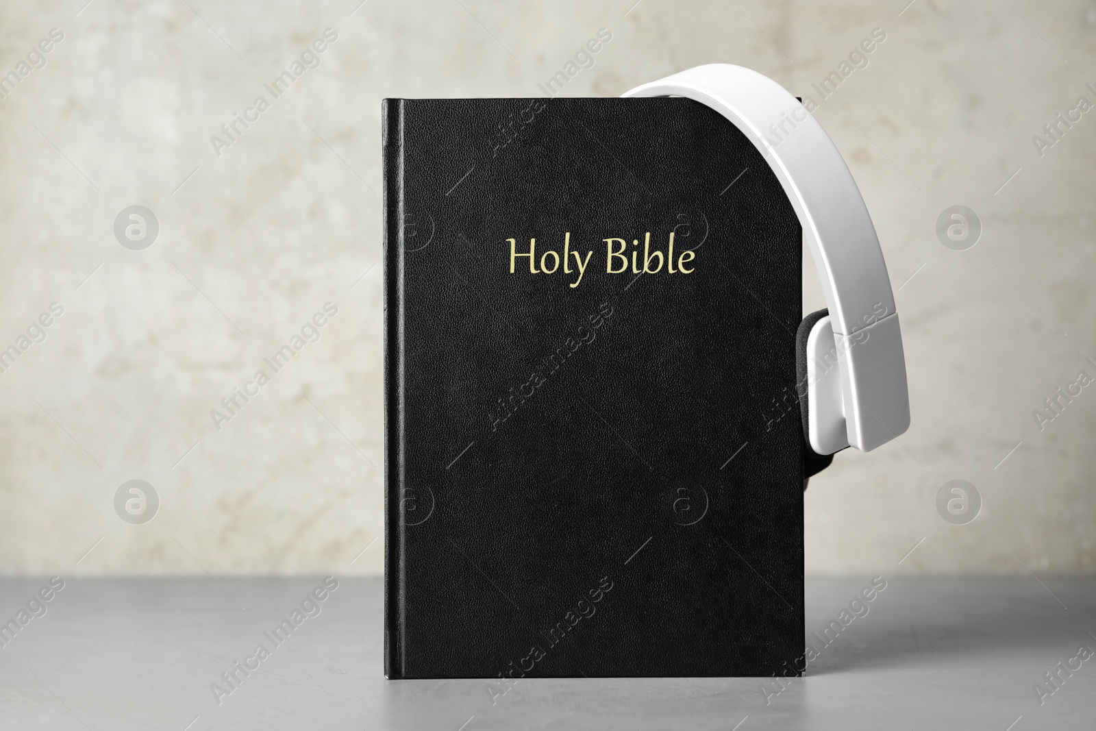 Photo of Bible and headphones on table against light grey background. Religious audiobook