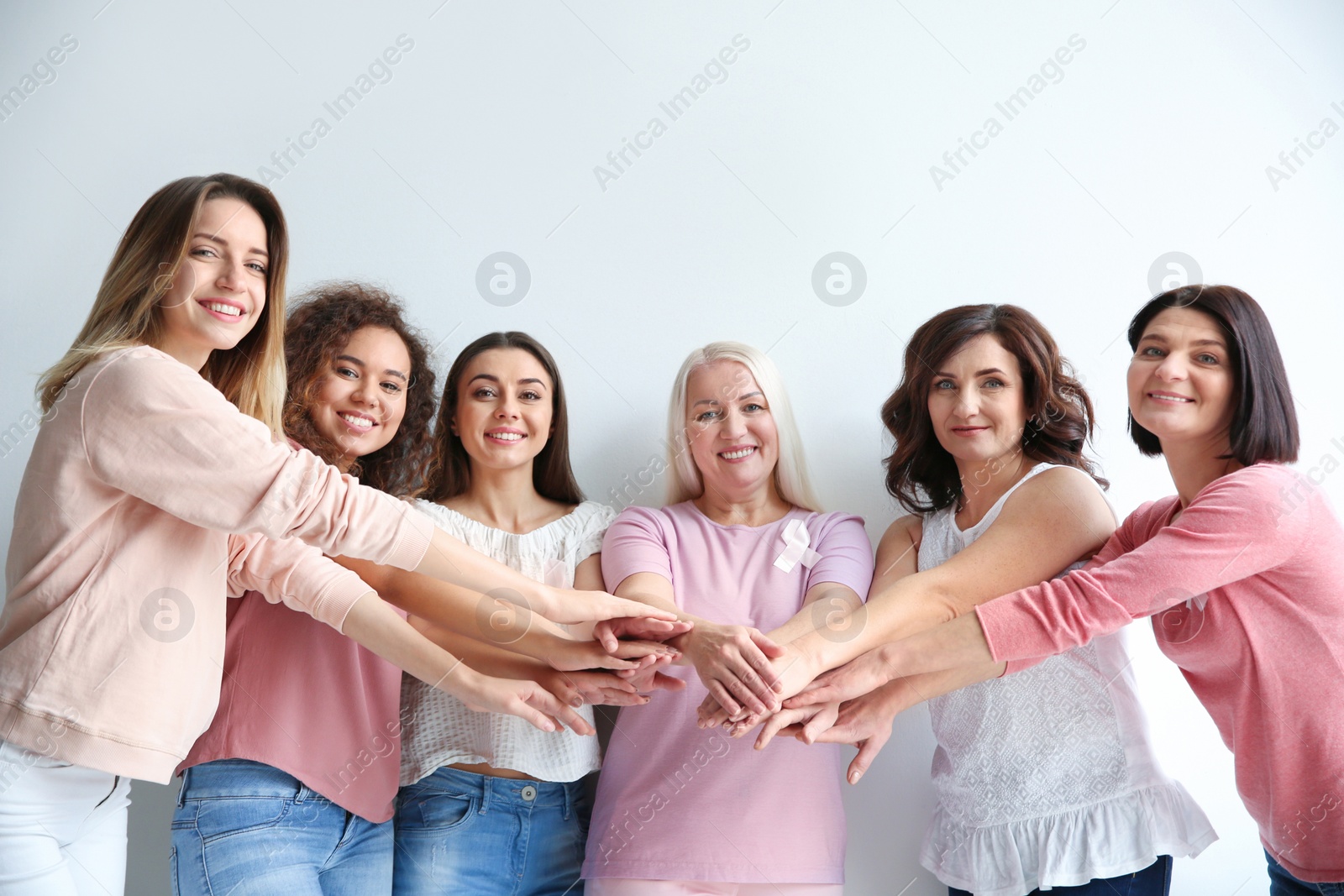 Photo of Group of women with silk ribbons joining hands against white background. Breast cancer awareness concept