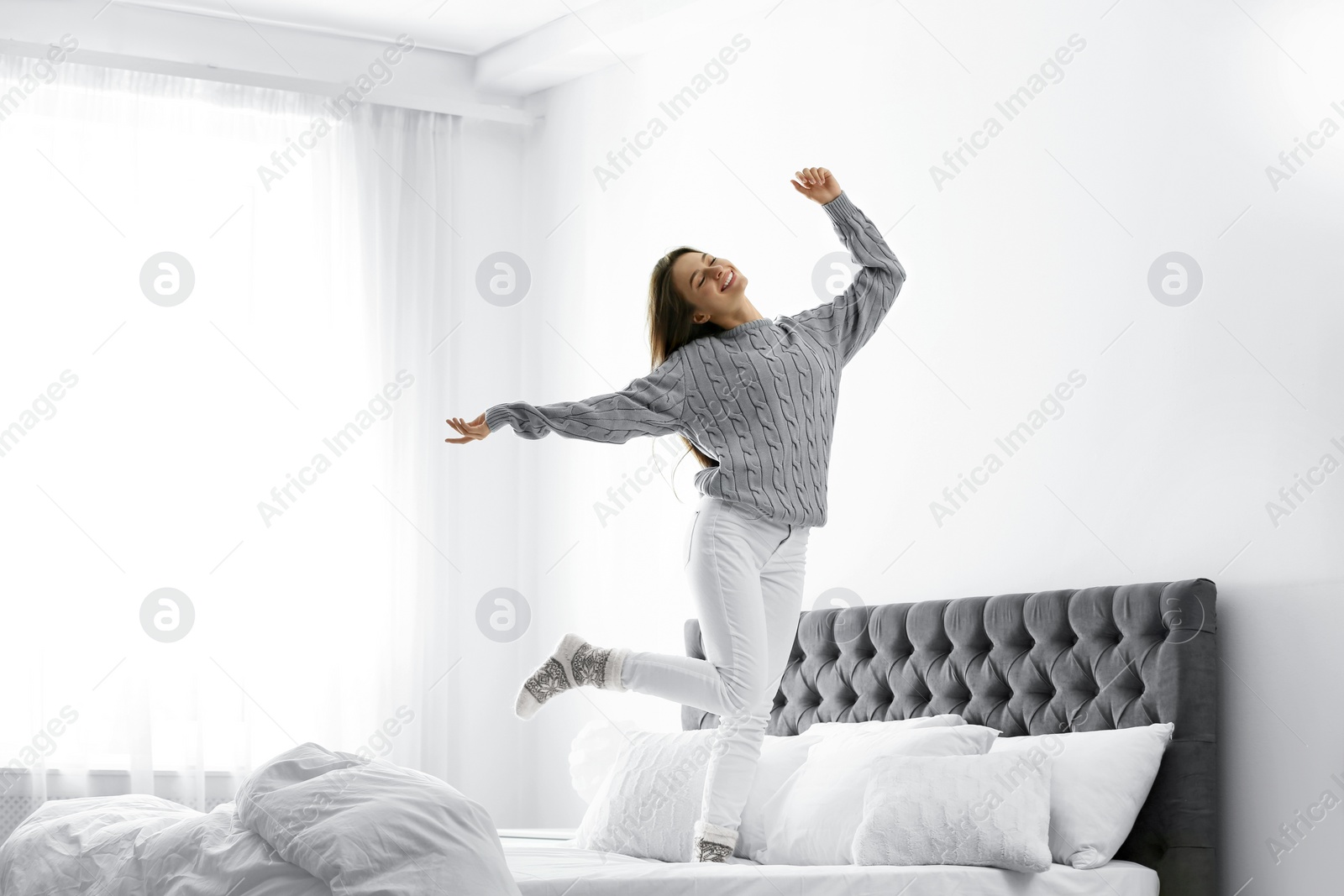 Photo of Young woman in warm sweater jumping on bed at home