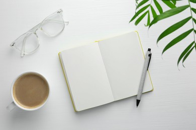 Open notebook, pen, glasses and cup of coffee on white wooden table, flat lay. Space for text