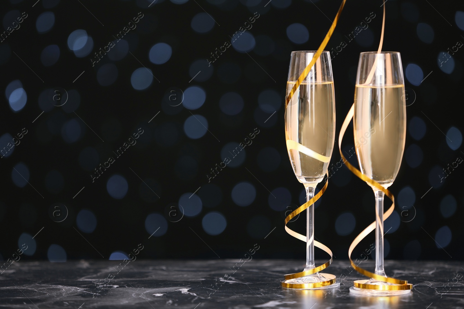 Photo of Glasses with champagne and space for text against blurred Christmas lights