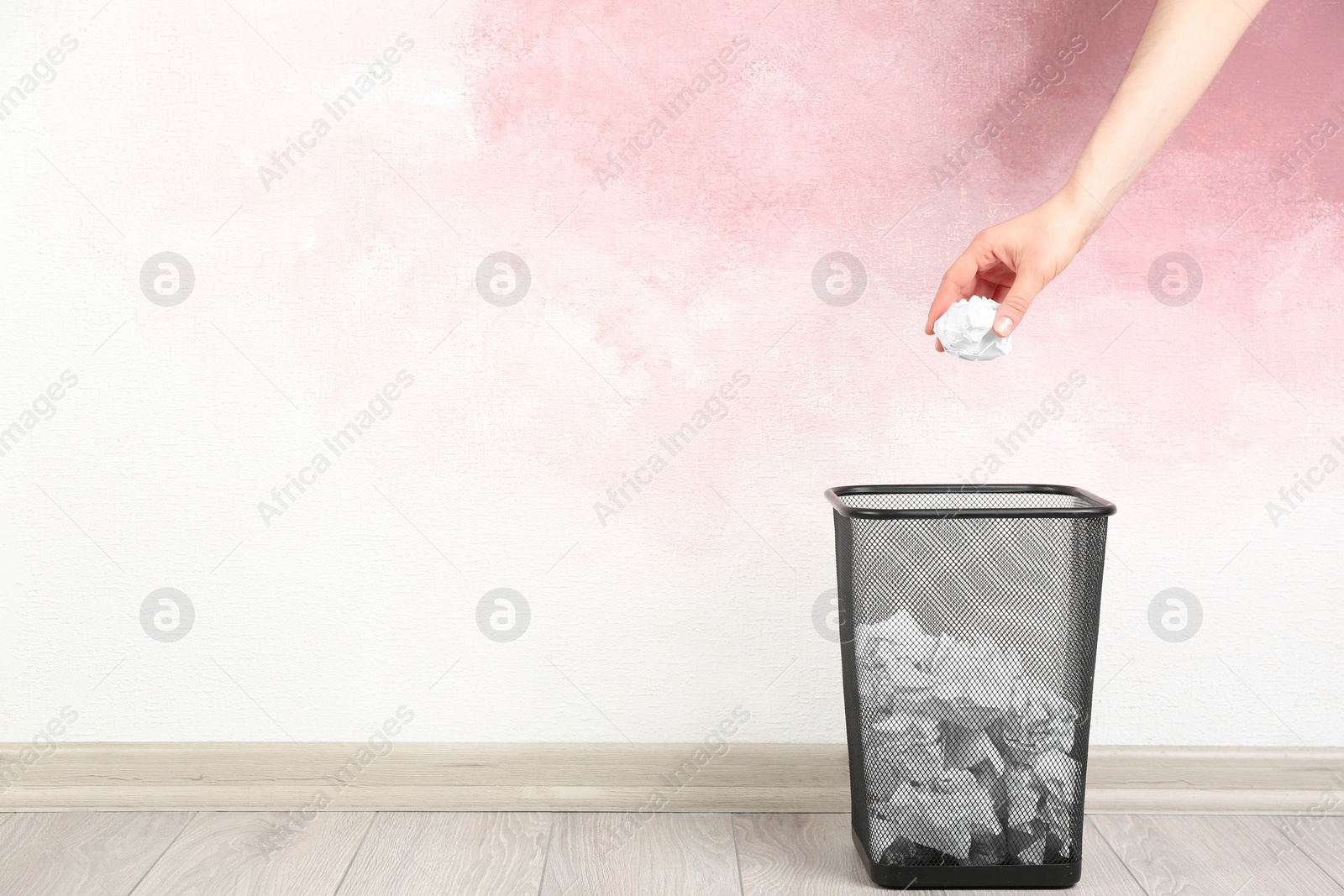 Photo of Woman throwing crumpled paper ball into basket near pink wall, closeup. Space for text