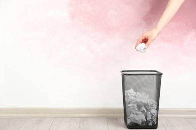 Woman throwing crumpled paper ball into basket near pink wall, closeup. Space for text