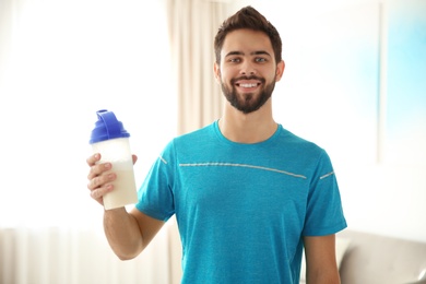Young sporty man with bottle of protein shake at home
