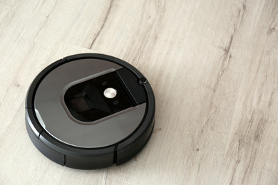 Photo of Modern robotic vacuum cleaner on wooden floor. Space for text