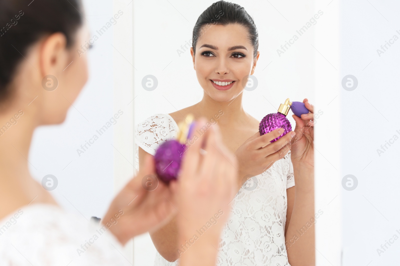 Photo of Young woman with bottle of perfume near mirror indoors