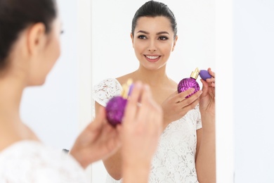 Young woman with bottle of perfume near mirror indoors