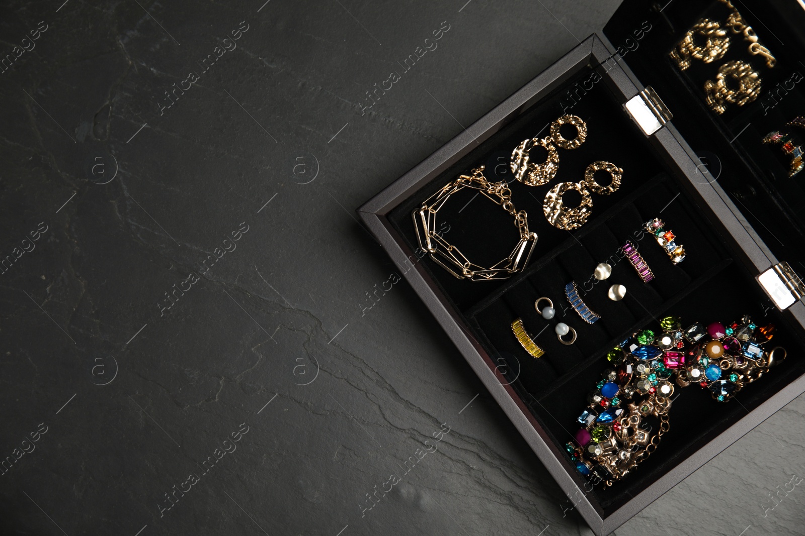 Photo of Jewelry box with stylish bijouterie on black table, top view. Space for text