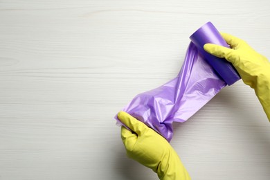 Photo of Janitor in rubber gloves holding roll of violet garbage bags over white wooden table, top view. Space for text