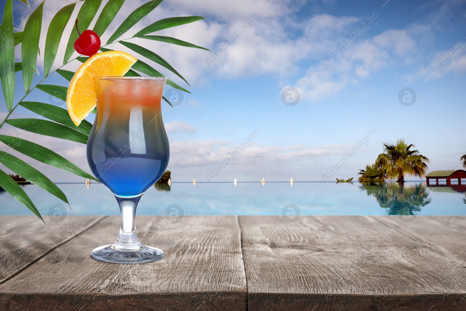 Image of Tasty cocktail on wooden table near outdoor swimming pool, space for text