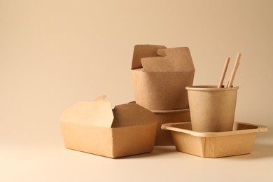 Photo of Eco friendly food packaging. Paper containers and tableware on beige background, space for text