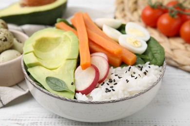 Delicious poke bowl with basil, eggs, avocado and vegetables on white wooden table, closeup