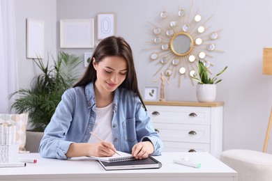 Photo of Young woman drawing in sketchbook at home, space for text