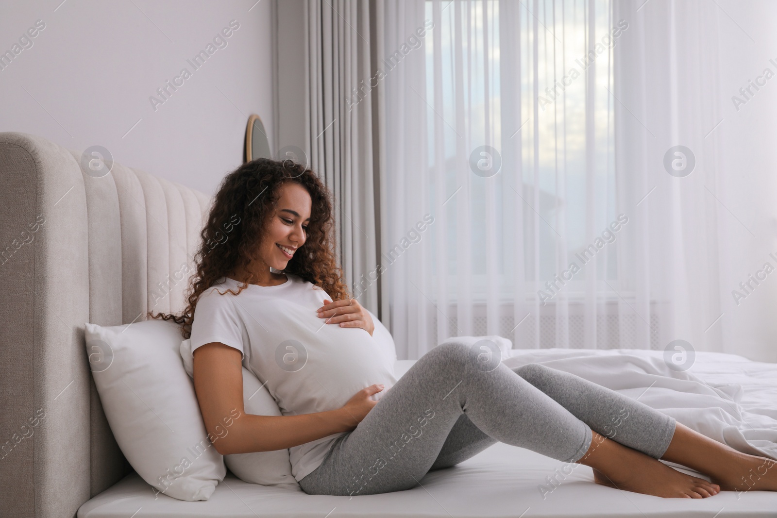 Photo of Pregnant young African-American woman sitting on bed at home