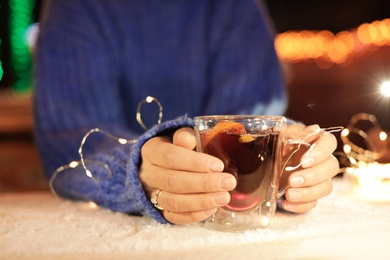 Woman with cup of mulled wine and garland at snowy table, closeup