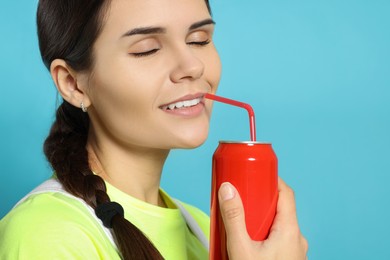 Photo of Beautiful woman drinking from red beverage can on light blue background, closeup