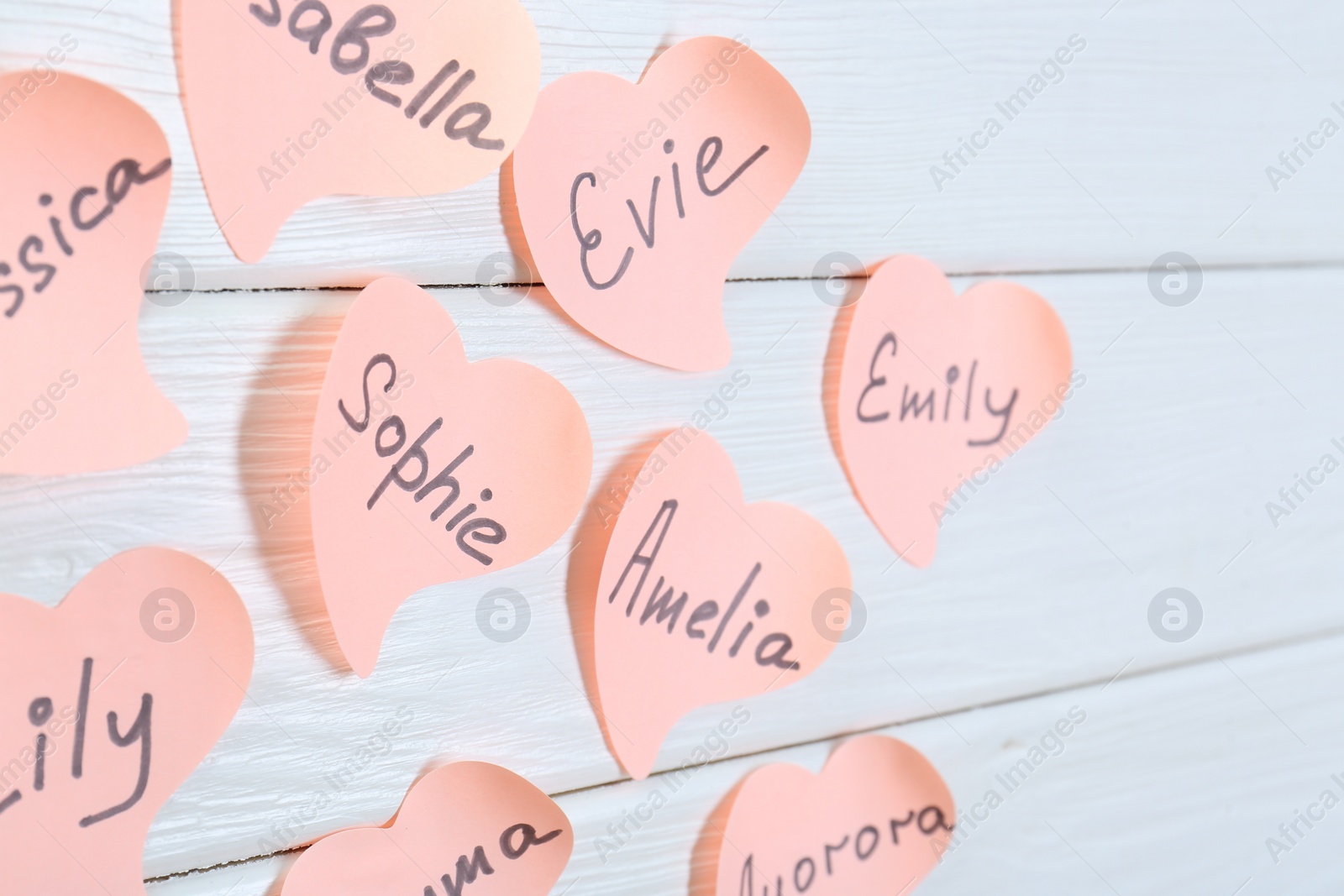 Photo of Paper stickers with different names on white wooden table, closeup. Choosing baby's name