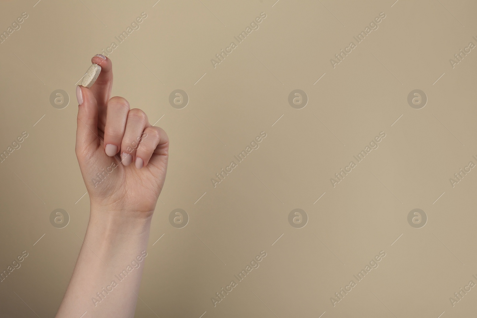 Photo of Woman holding vitamin pill on dark beige background, closeup with space for text. Health supplement