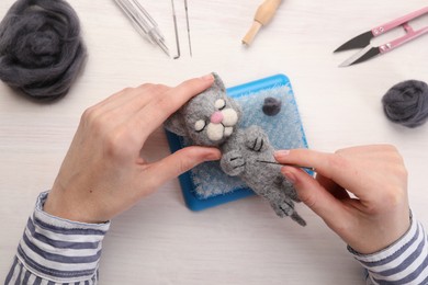 Photo of Woman felting toy cat from wool at light wooden table, top view