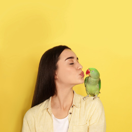 Photo of Young woman with Alexandrine parakeet on yellow background, space for text. Cute pet