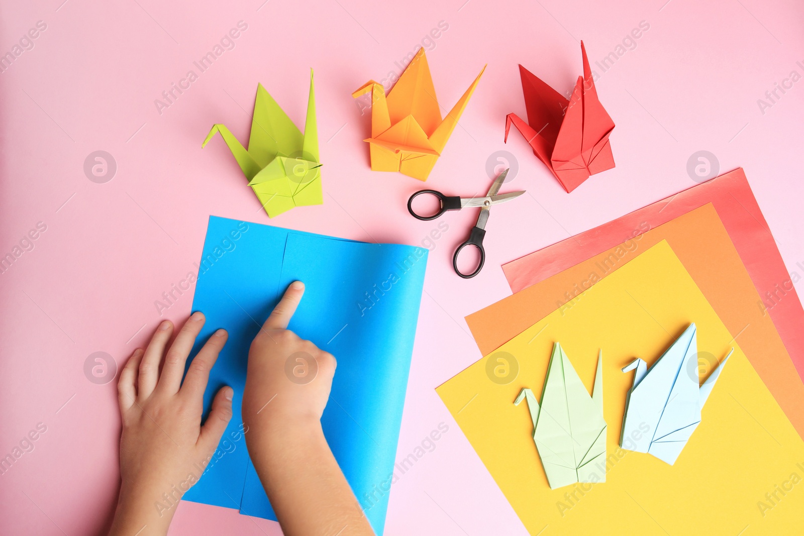 Photo of Origami art. Child folding paper on pink background, closeup and top view
