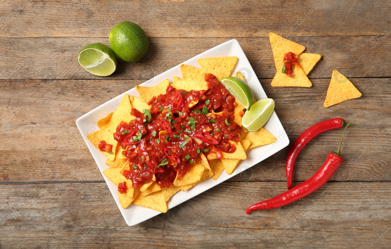 Photo of Plate of delicious mexican nachos chips with salsa sauce, lime and chili peppers on wooden table, flat lay