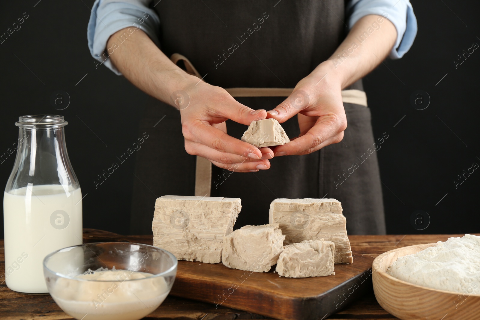 Photo of Woman with compressed yeast and dough ingredients at wooden table, closeup
