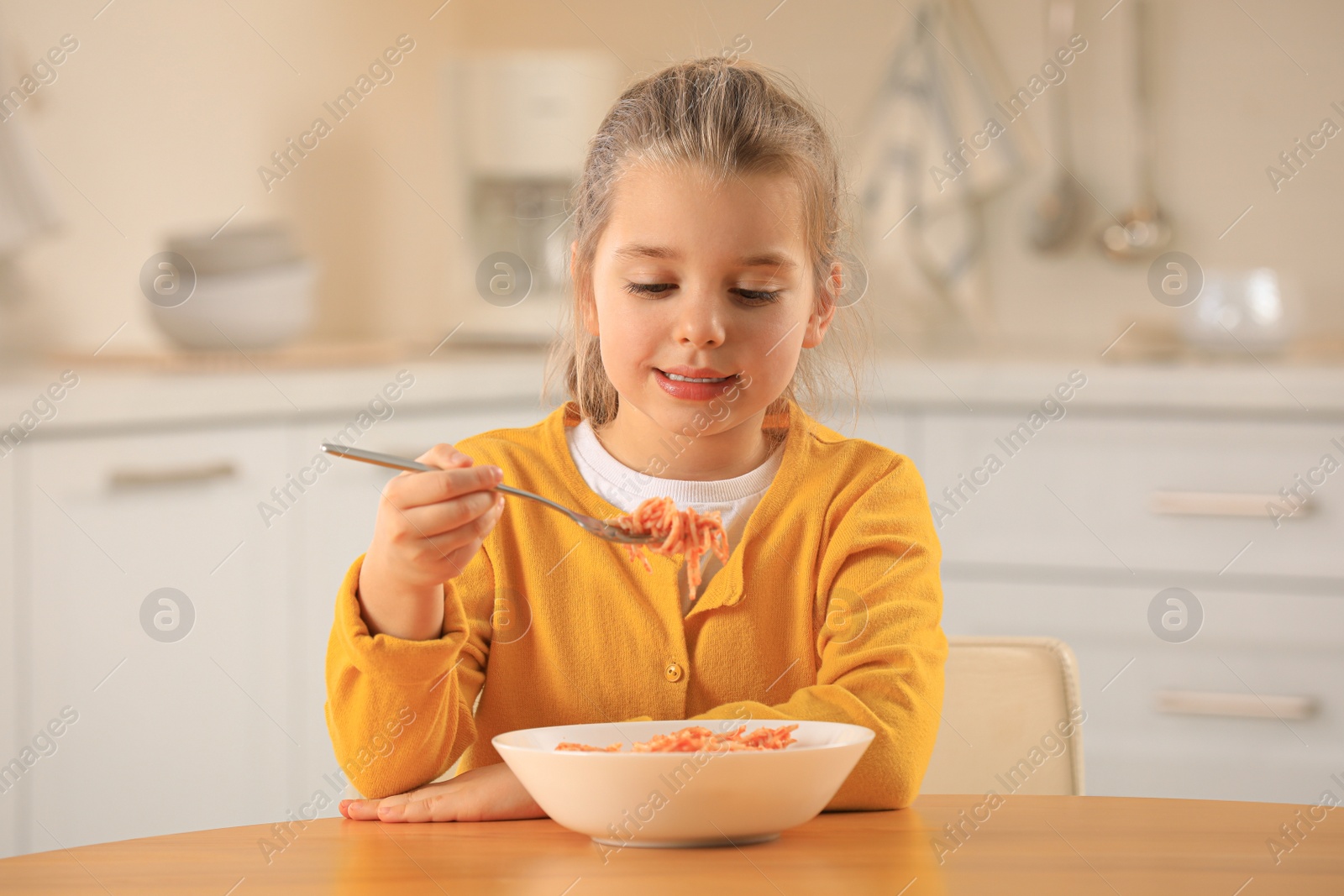 Photo of Cute little girl eating tasty pasta at table in kitchen