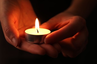 Photo of Woman with burning candle in darkness, closeup. Memory day