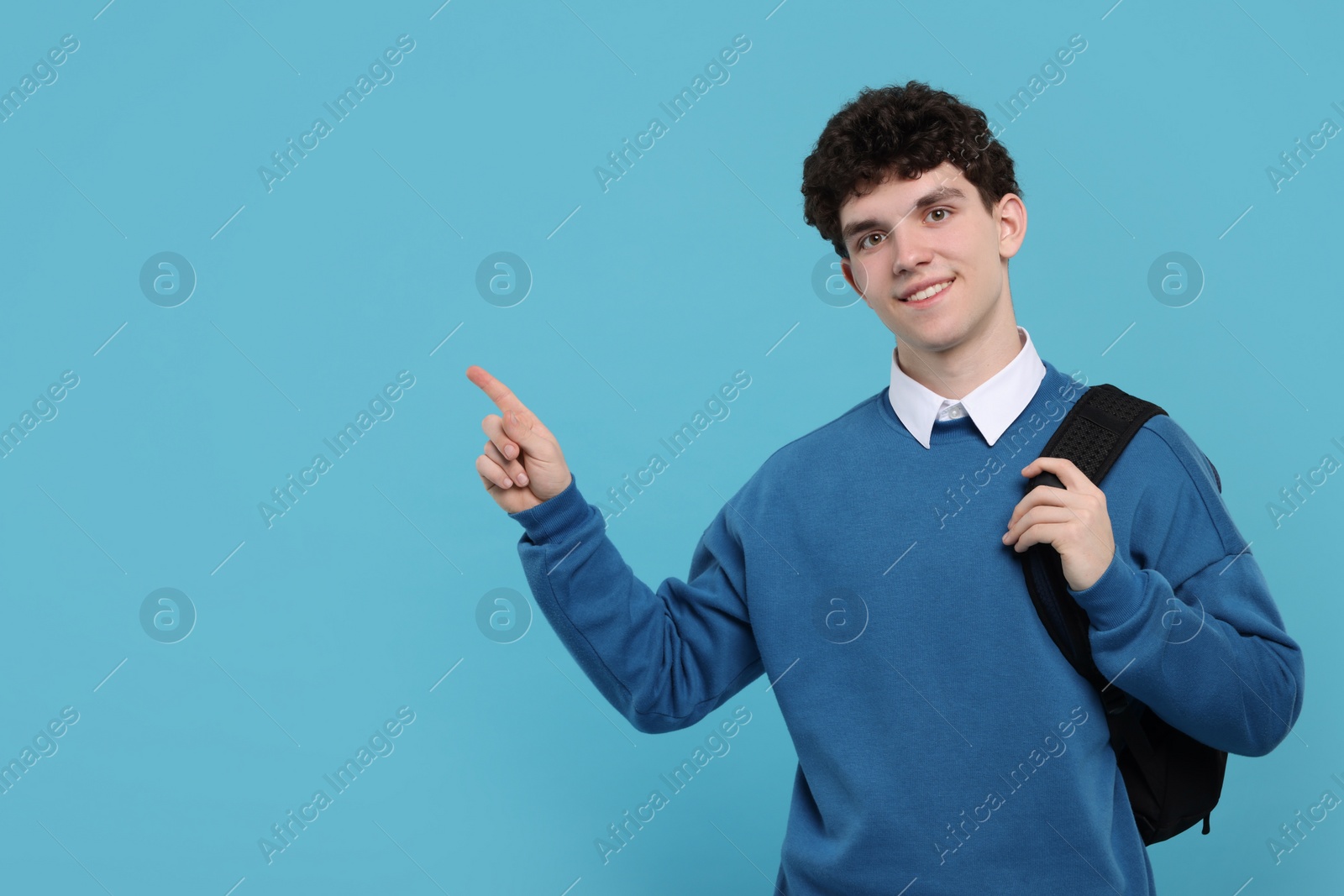 Photo of Portrait of student with backpack pointing on light blue background. Space for text