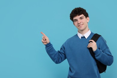 Portrait of student with backpack pointing on light blue background. Space for text