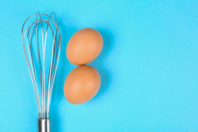 Photo of Raw eggs and whisk on light blue background,  top view with space for text. Baking pie