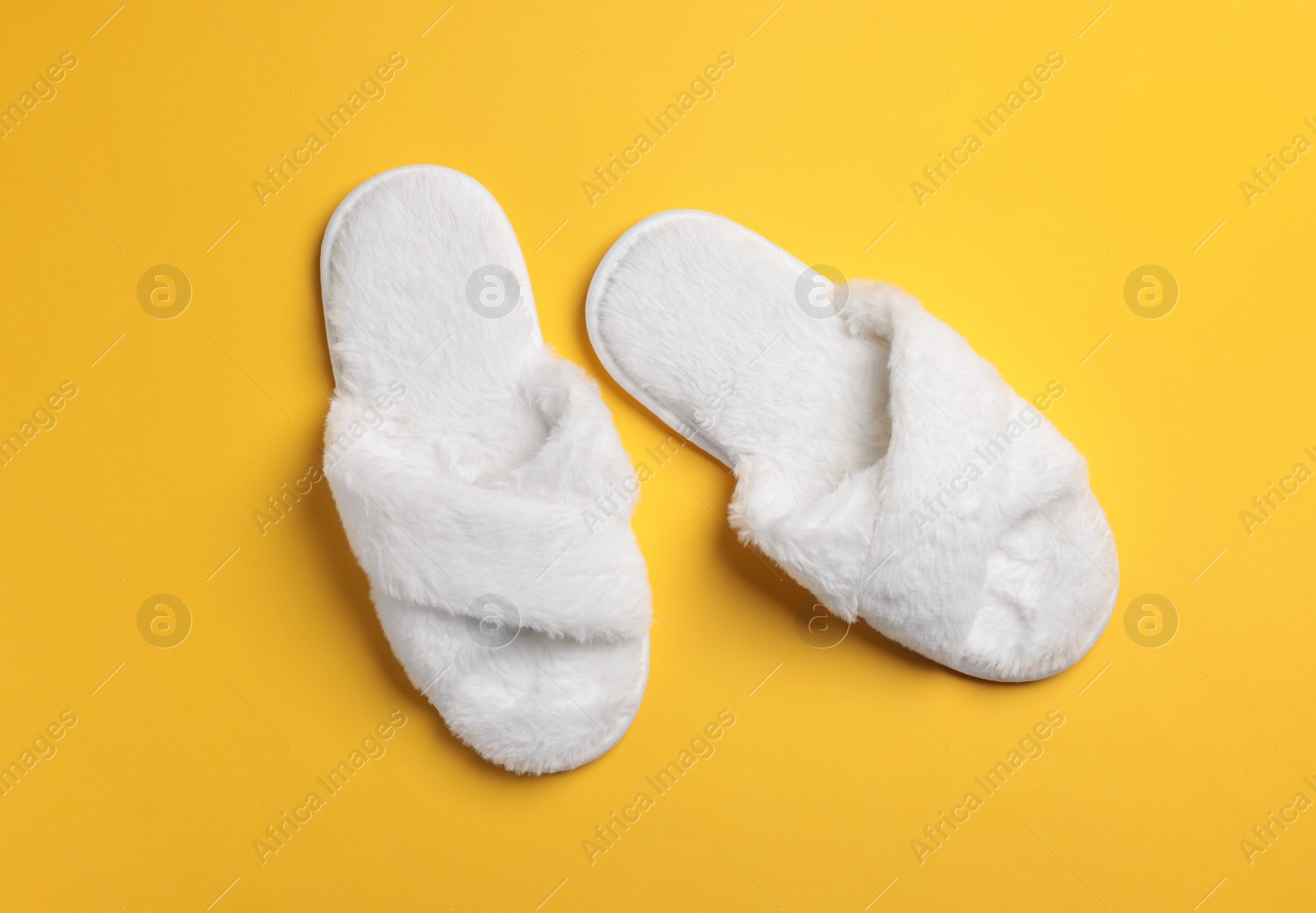 Photo of Pair of soft fluffy slippers on yellow background, top view