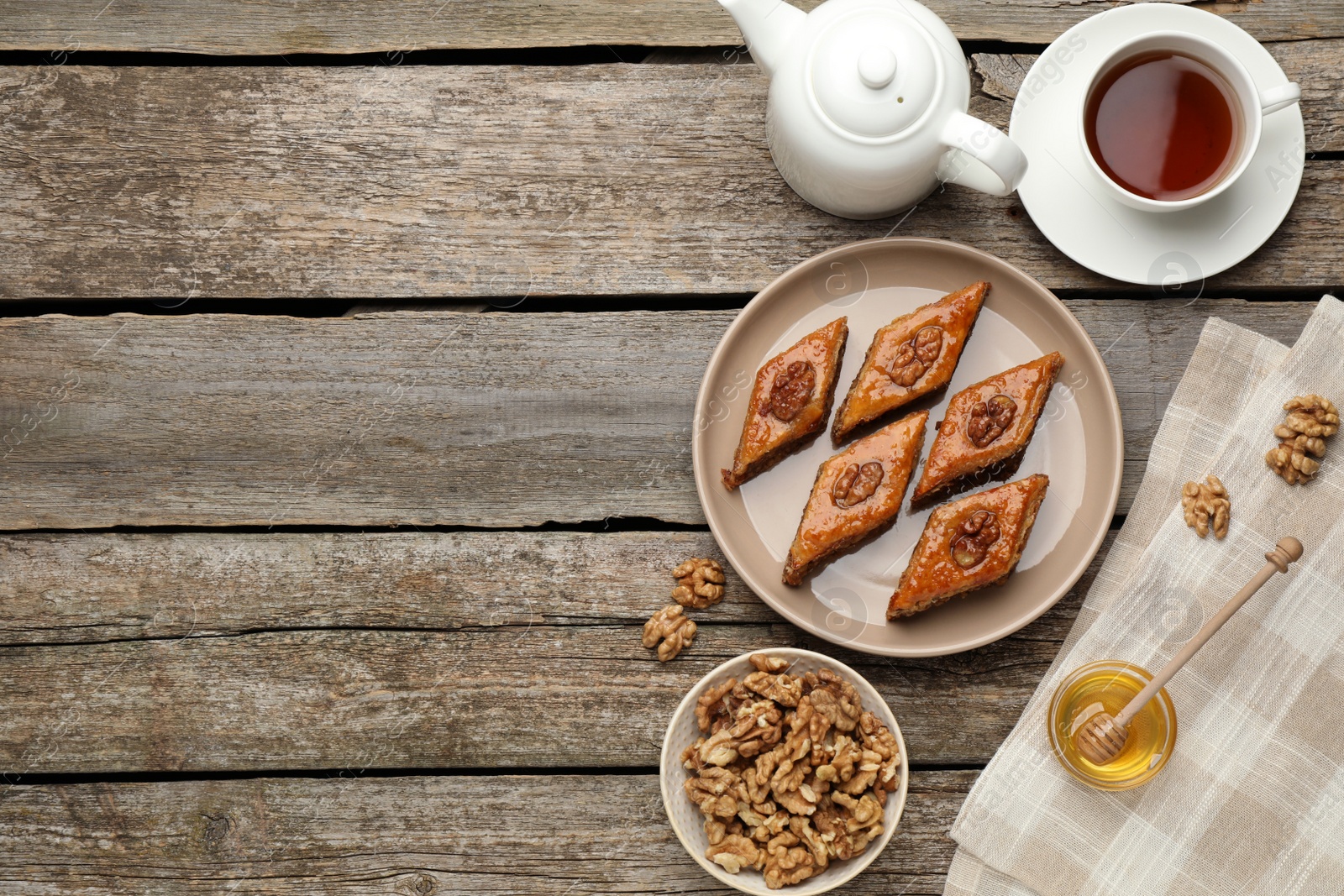 Photo of Delicious sweet baklava with walnuts, honey and hot tea on wooden table, flat lay. Space for text