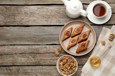 Photo of Delicious sweet baklava with walnuts, honey and hot tea on wooden table, flat lay. Space for text