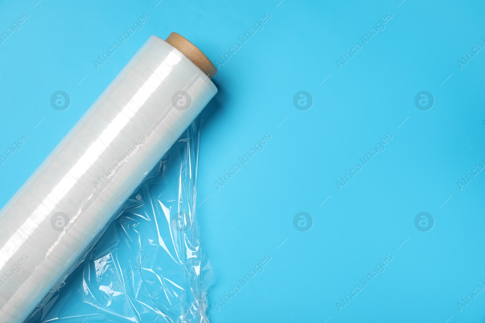 Photo of Roll of transparent stretch wrap on turquoise background, top view. Space for text