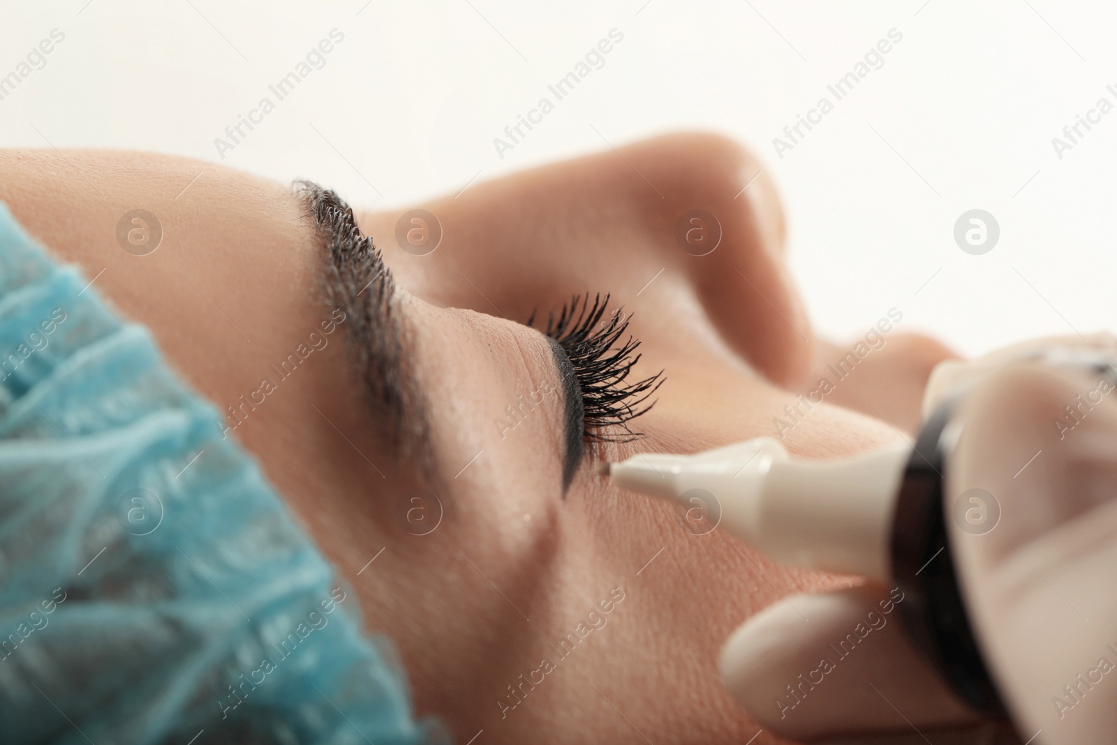 Photo of Young woman undergoing procedure of permanent eyeliner makeup on white background, closeup