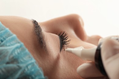 Young woman undergoing procedure of permanent eyeliner makeup on white background, closeup