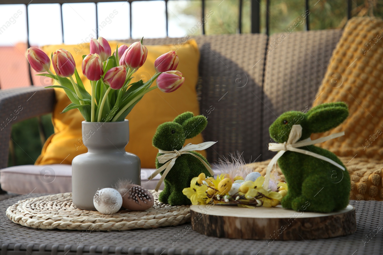 Photo of Terrace with Easter decorations. Bouquet of tulips in vase, bunny figures, decorative nest and eggs on table outdoors