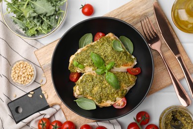 Delicious chicken breasts with pesto sauce, ingredients and cutlery on white table, flat lay