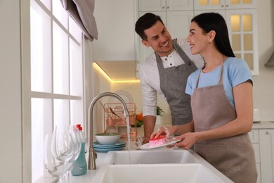 Photo of Happy lovely couple washing dishes in kitchen