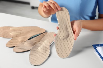 Photo of Female orthopedist showing insoles at table in hospital, closeup