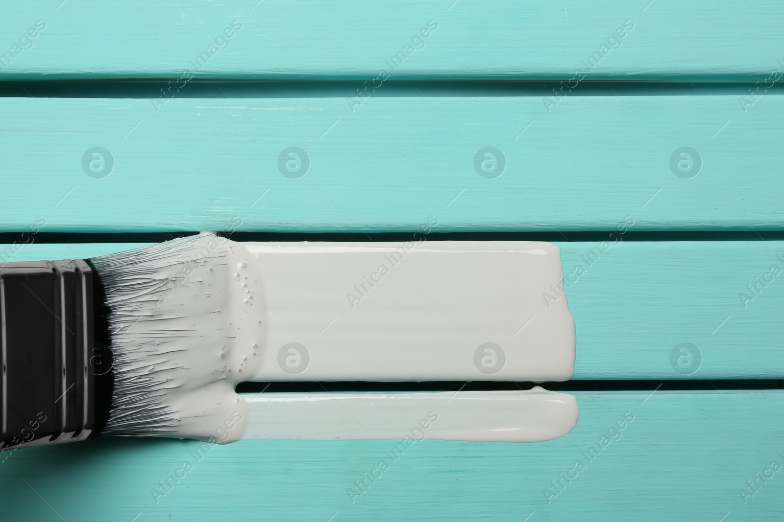 Photo of Brush and white paint stroke on blue wooden background, top view. Space for text