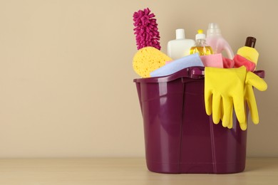 Photo of Bucket with different cleaning supplies on wooden floor near beige wall. Space for text
