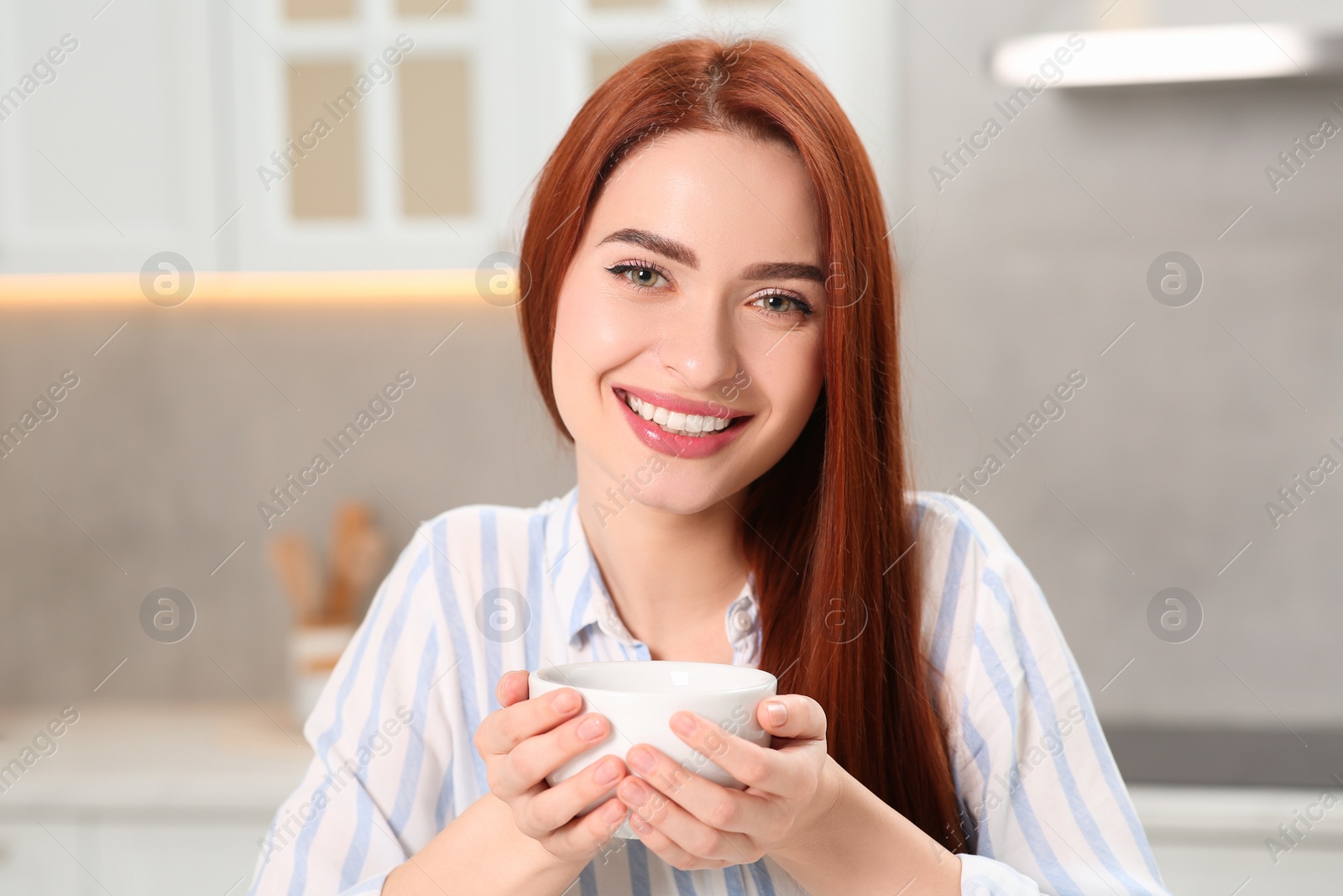 Photo of Happy woman with red dyed hair holding cup of drink in kitchen