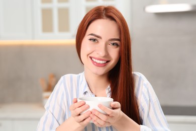 Photo of Happy woman with red dyed hair holding cup of drink in kitchen