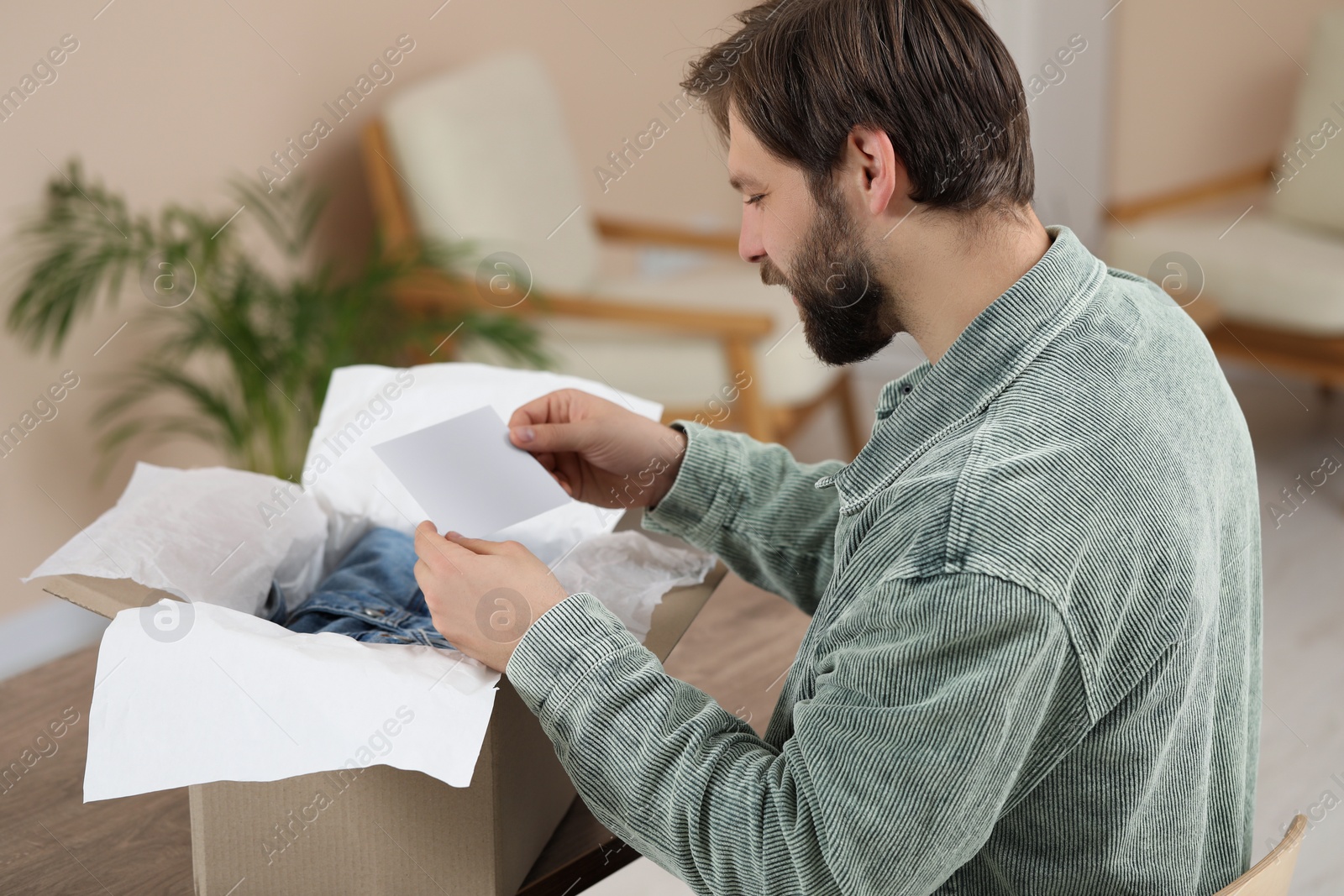 Photo of Man with greeting card near parcel at home. Internet shopping